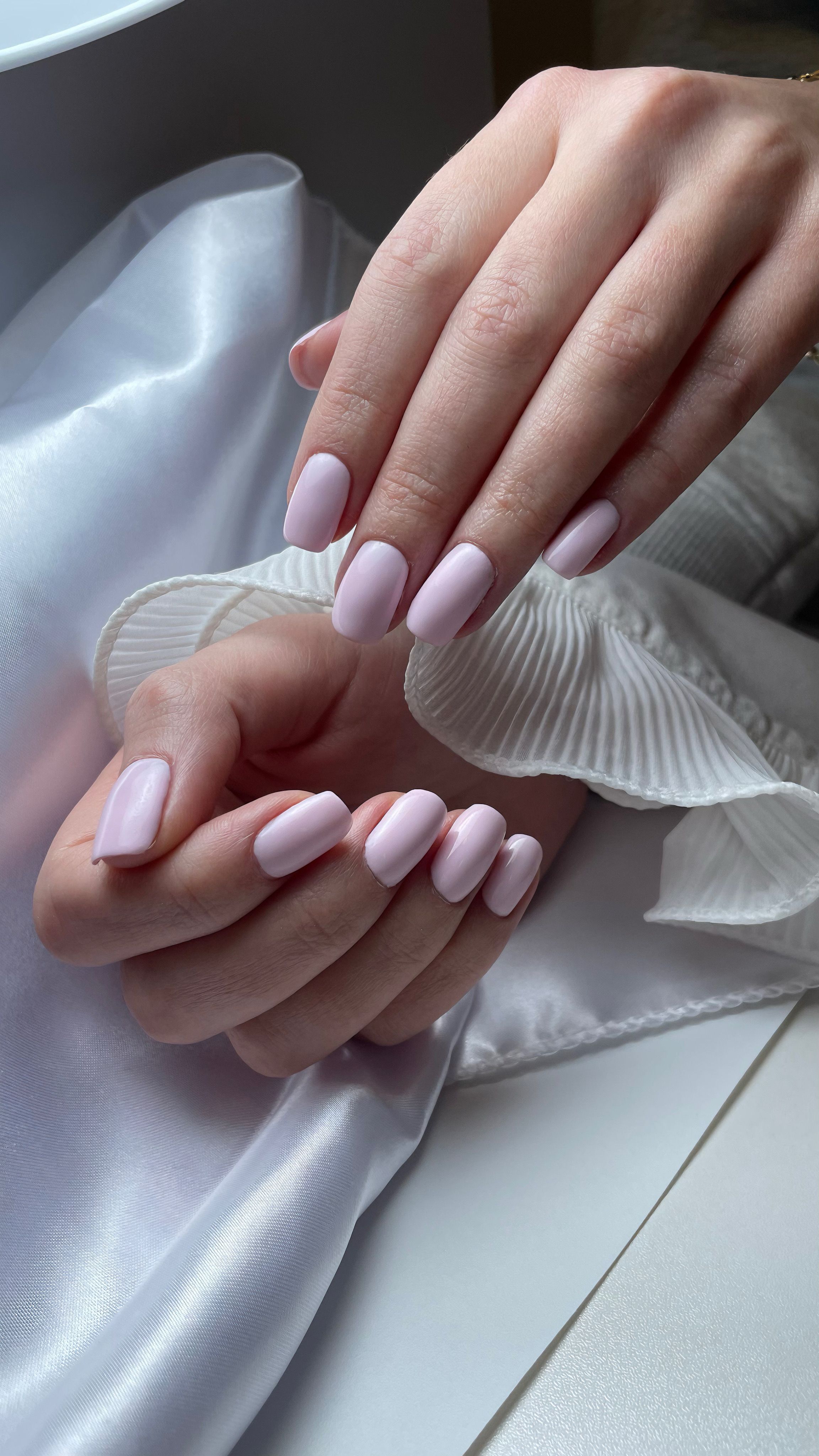 Elegante gepflegte Frauenhände mit rosa Maniküre auf seidigem Stoff